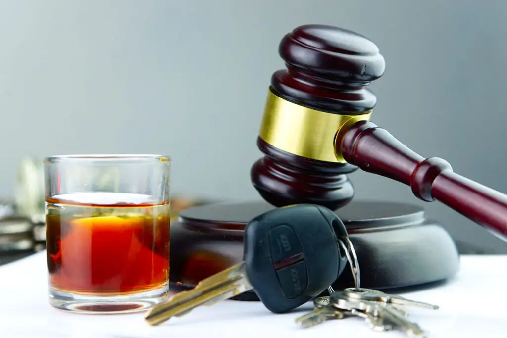 a glass with liquor, car keys, and a wooden gavel with sound block is on top of a white table.