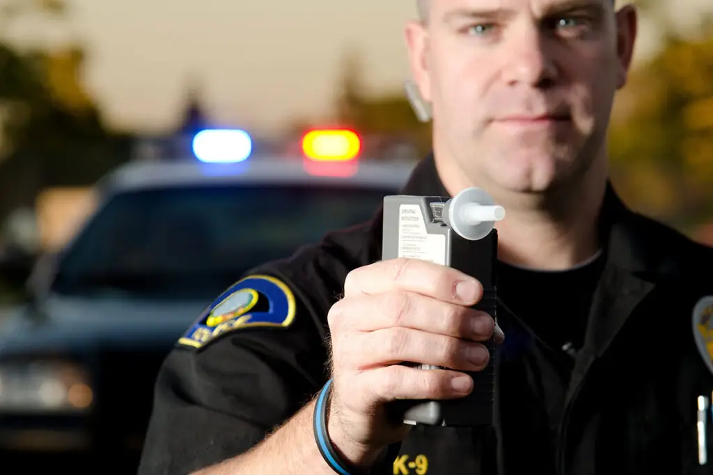 A police officer holding a breathalyzer and reaching out to a driver.