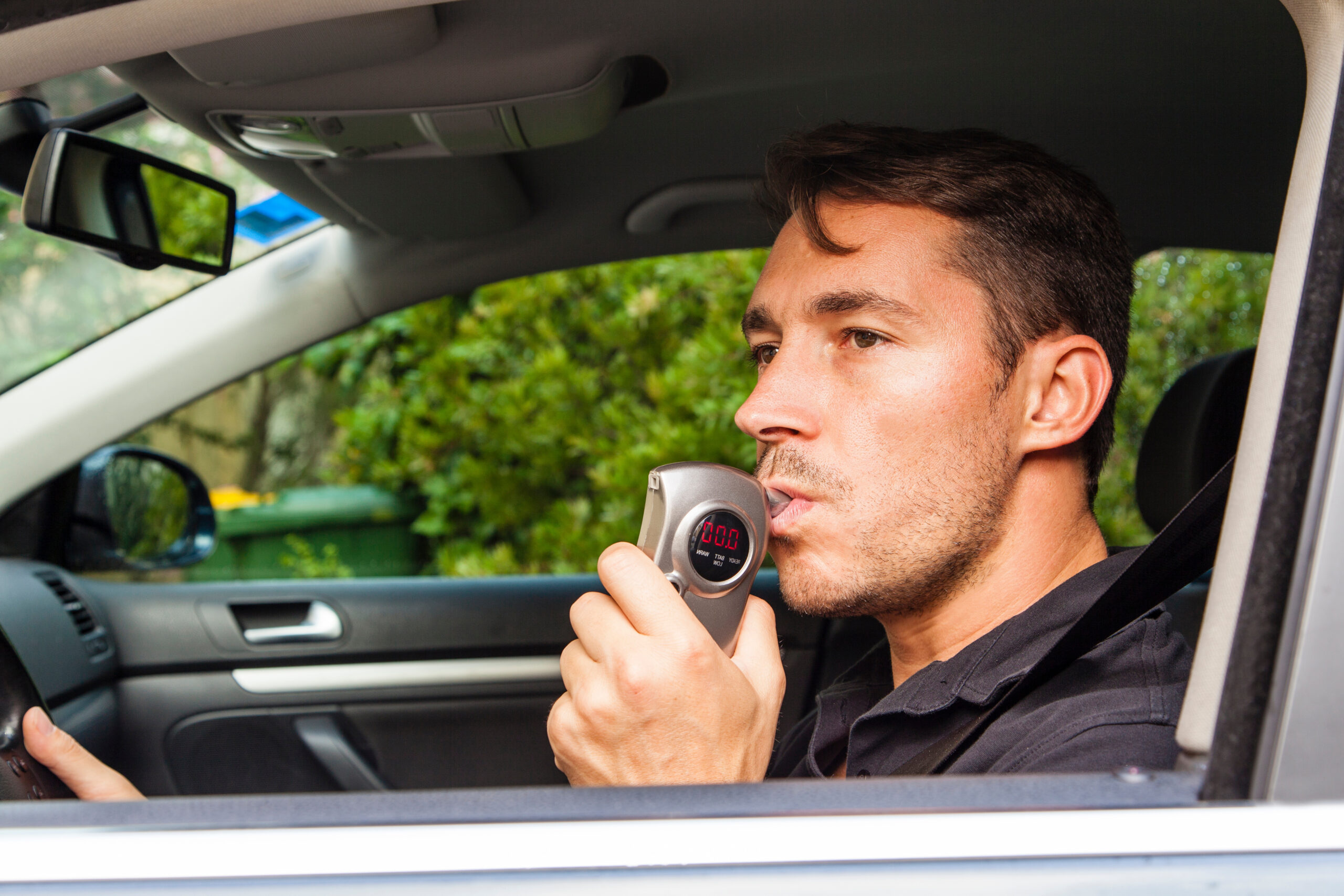 Man in car blowing into breathalyzer.